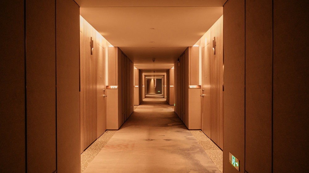 Couloir d’hôtel aux murs clairs, portes en bois et éclairage chaud.