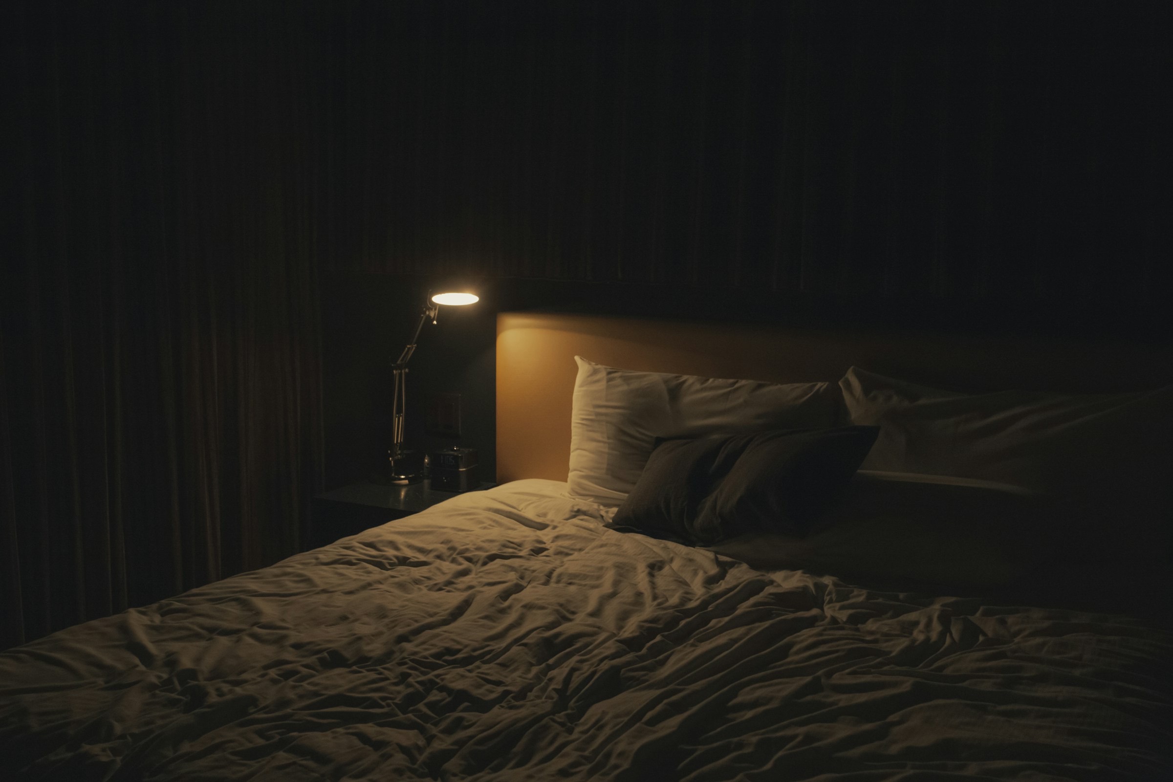 Chambre plongée dans la nuit, lit défait éclairé par une lampe de chevet.